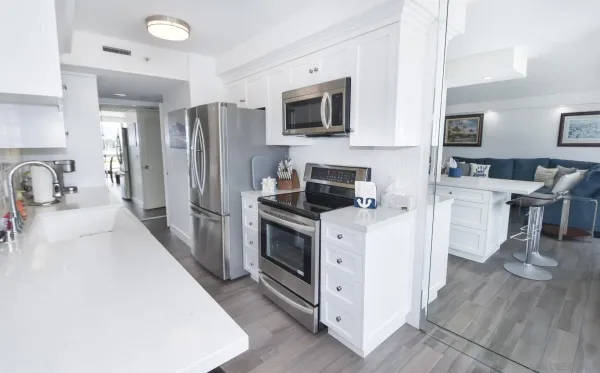 a kitchen with stainless steel appliances a stove top oven a sink a refrigerator white cabinets and wooden floor