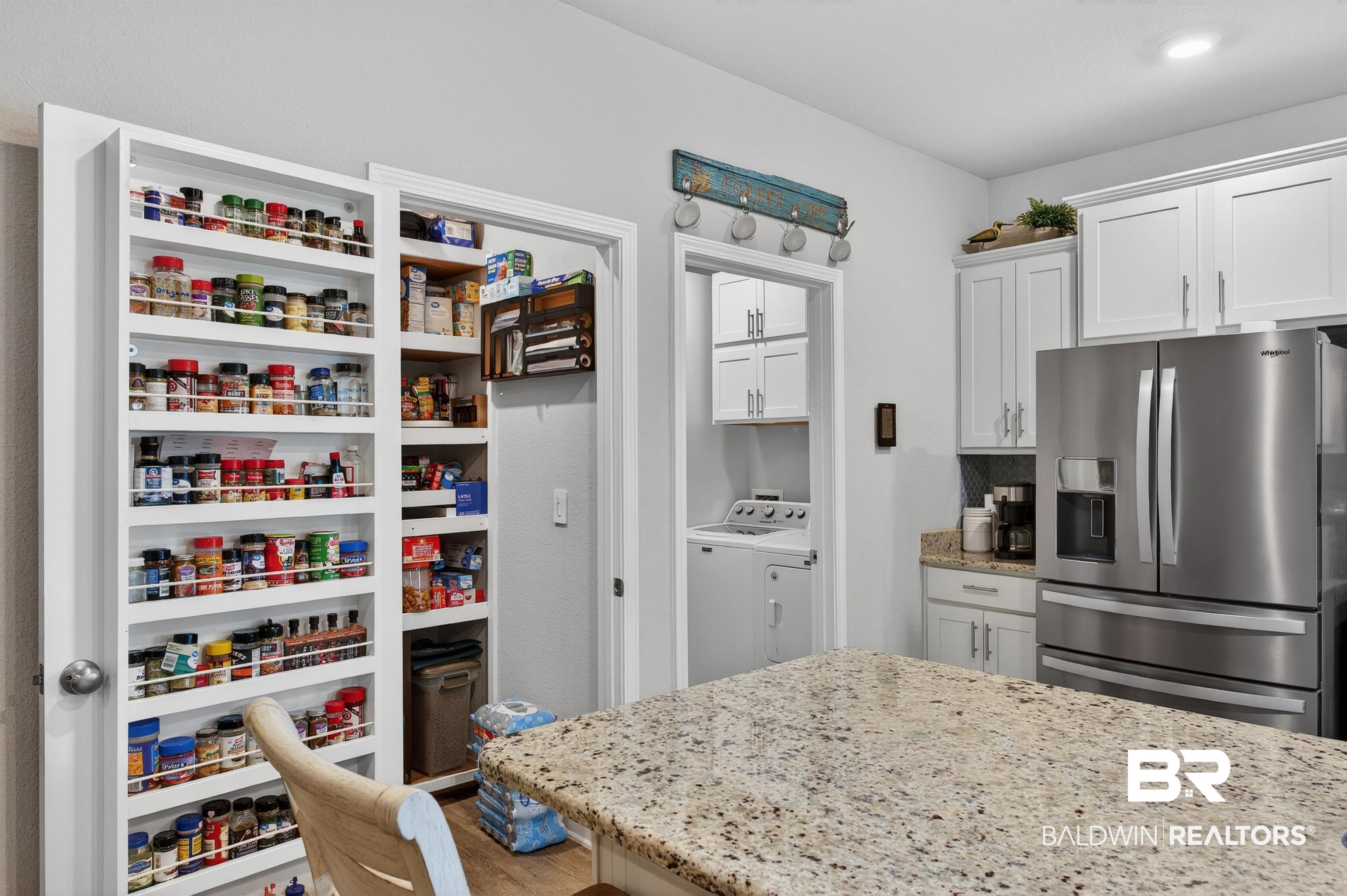 8735 Bronze Lane Foley, AL 36535 - Photo 13 of 58 Spacious kitchen featuring a large pantry with built-in shelving, stainless steel refrigerator, white shaker-style cabinetry, and a substantial island with a speckled countertop