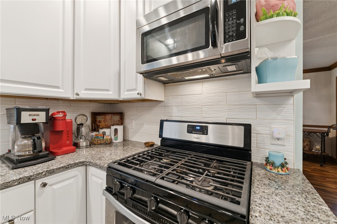 6930 Firestone Road Northeast Canton, OH 44721 - Photo 12 of 49 Kitchen featuring stainless steel appliances, white cabinetry, light stone countertops, decorative backsplash, and crown molding