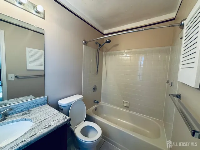 a bathroom with a granite countertop bathtub shower sink vanity and toilet