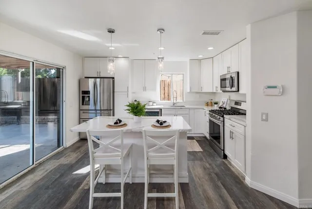 a kitchen with stainless steel appliances kitchen island granite countertop a refrigerator a stove a sink dishwasher and a dining table with wooden floor