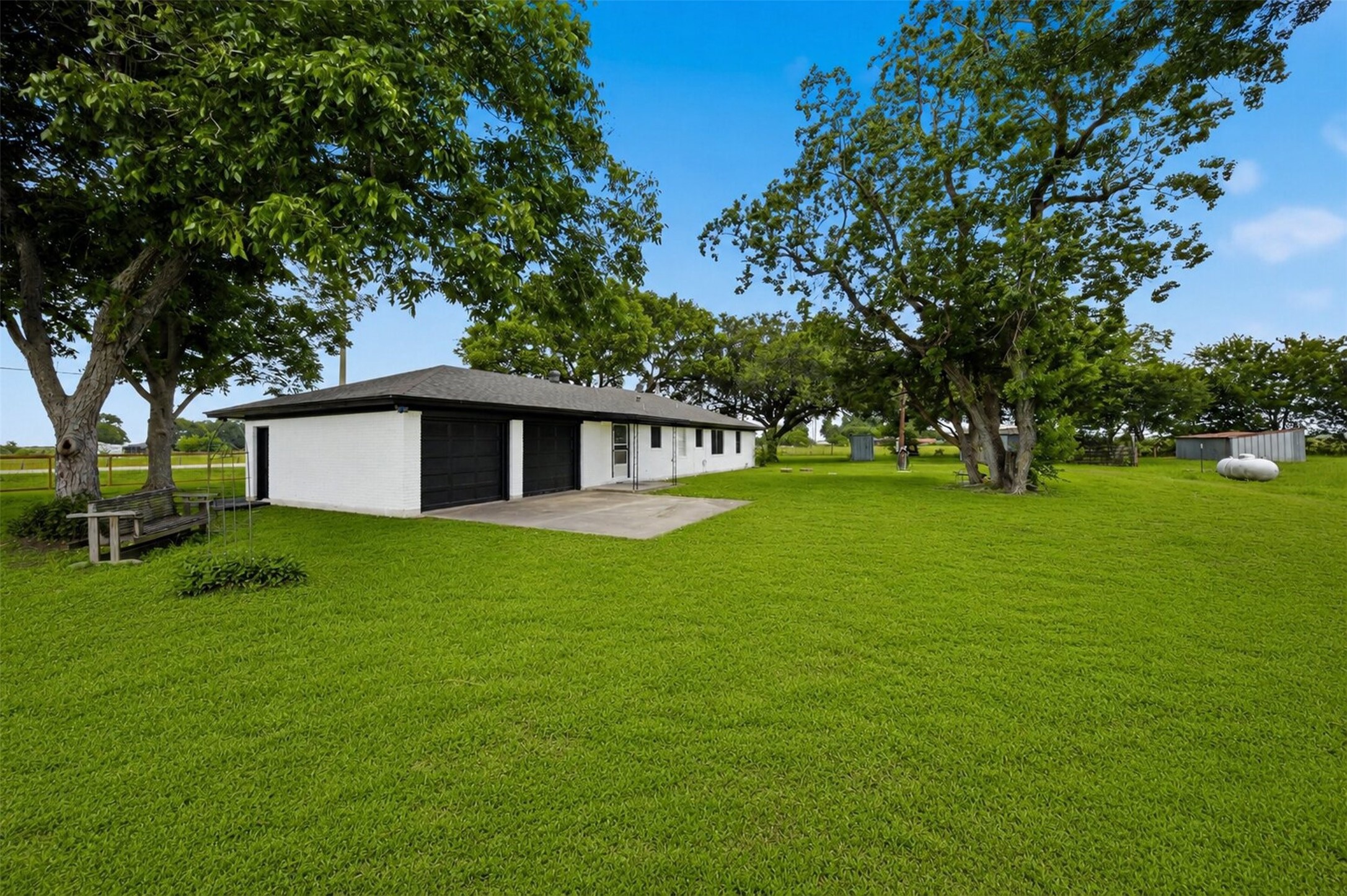 5443 Randon School Road Rosenberg, TX 77471 - Photo 19 of 20 Rear elevation view showing the attached garage, black garage doors, concrete drive area, mature trees, and expansive green lawn.