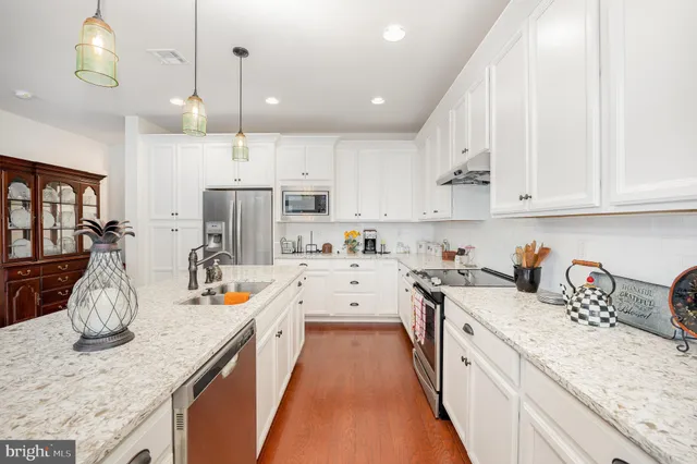 a kitchen with stainless steel appliances granite countertop a sink stove and white cabinets with wooden floor