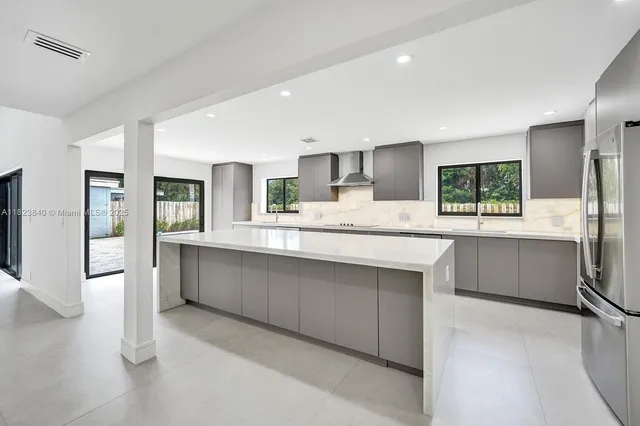 a large kitchen with stainless steel appliances a large counter top a refrigerator and cabinets