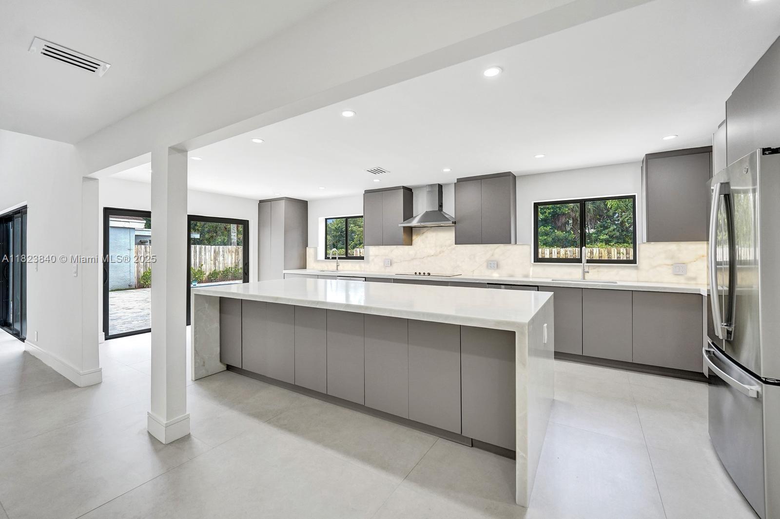 a large kitchen with stainless steel appliances a large counter top a refrigerator and cabinets