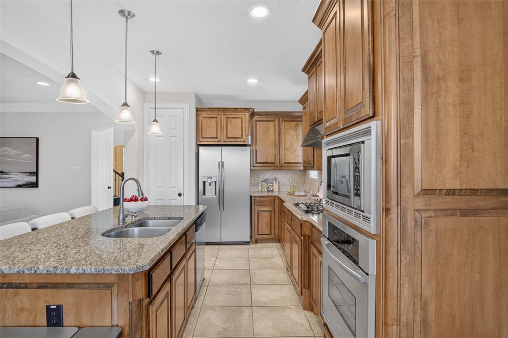 842 Sun Meadow Road Allen, TX 75013 - Photo 7 of 39 Kitchen with granite countertops, stainless steel appliances, ceramic tile flooring, wood-finish cabinetry, and pendant lighting