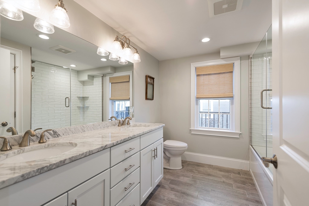 64 County Road, Unit 1 Ipswich, MA 01938 - Photo 22 of 33 a bathroom with a granite countertop sink toilet a mirror a vanity and shower