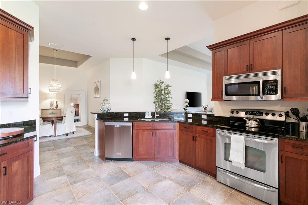7563 Moorgate Point Way Naples, FL 34113 - Photo 18 of 40 a kitchen with stainless steel appliances granite countertop a stove top oven a sink dishwasher a dining table and chairs with wooden floor