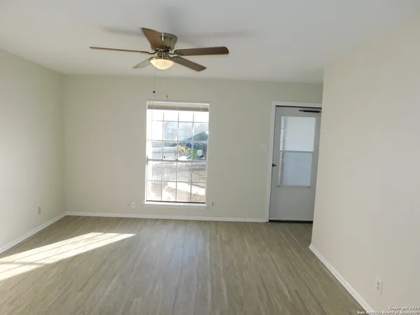 an empty room with wooden floor fan and windows