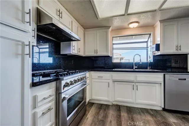 a kitchen with stainless steel appliances granite countertop a stove a sink and white cabinets