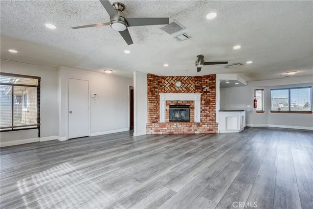 an empty room with wooden floor fireplace cabinet and windows