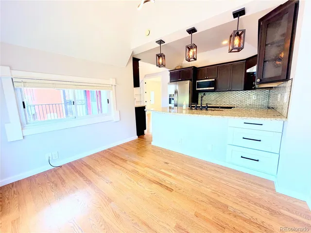 a room with kitchen island stainless steel appliances wooden floor and windows