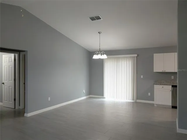 an empty room with chandelier fan and windows