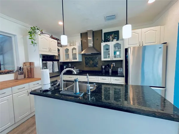 a kitchen with stainless steel appliances granite countertop a refrigerator a stove and a sink with wooden floor