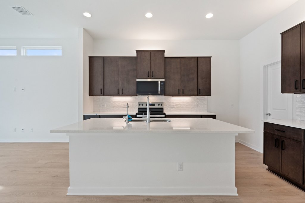 2205 Cento Walk Round Rock, TX 78664 - Photo 6 of 32 Kitchen featuring dark wood finish cabinets, tasteful backsplash, a center island with sink, stainless steel appliances, and recessed lighting