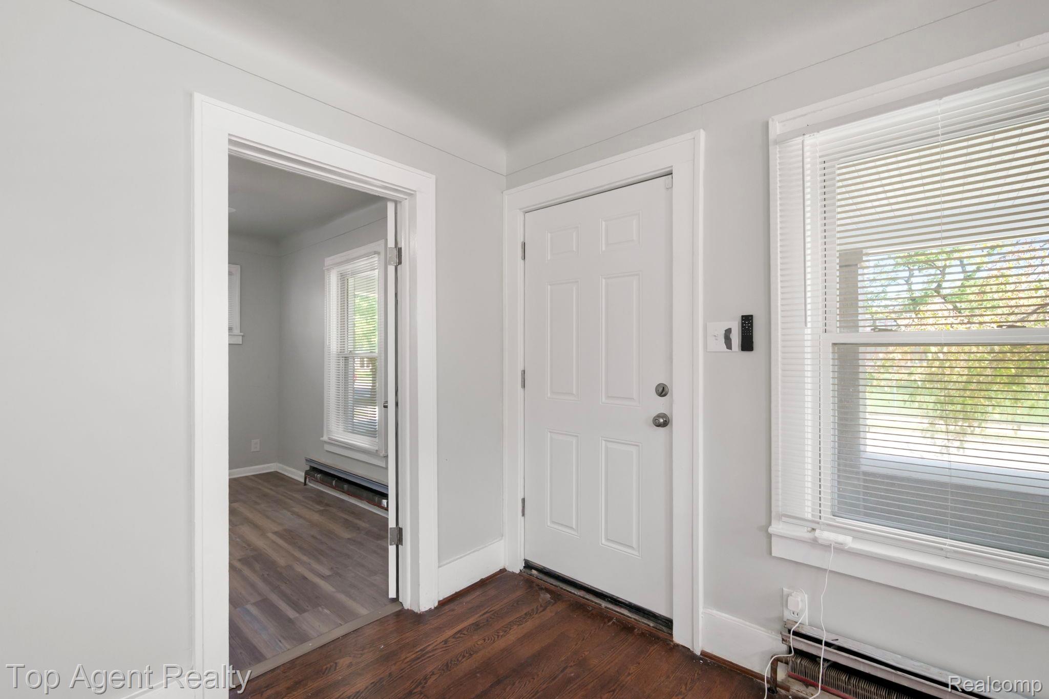 White paneled door, double-hung windows with blinds, and rich wood-finish flooring
