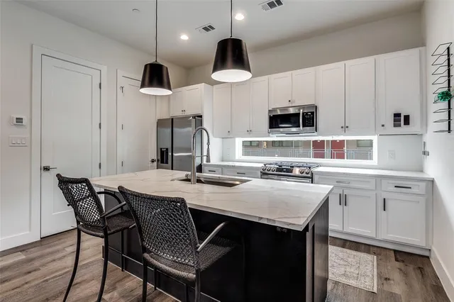 a kitchen with stainless steel appliances a stove a sink a microwave a refrigerator and white cabinets