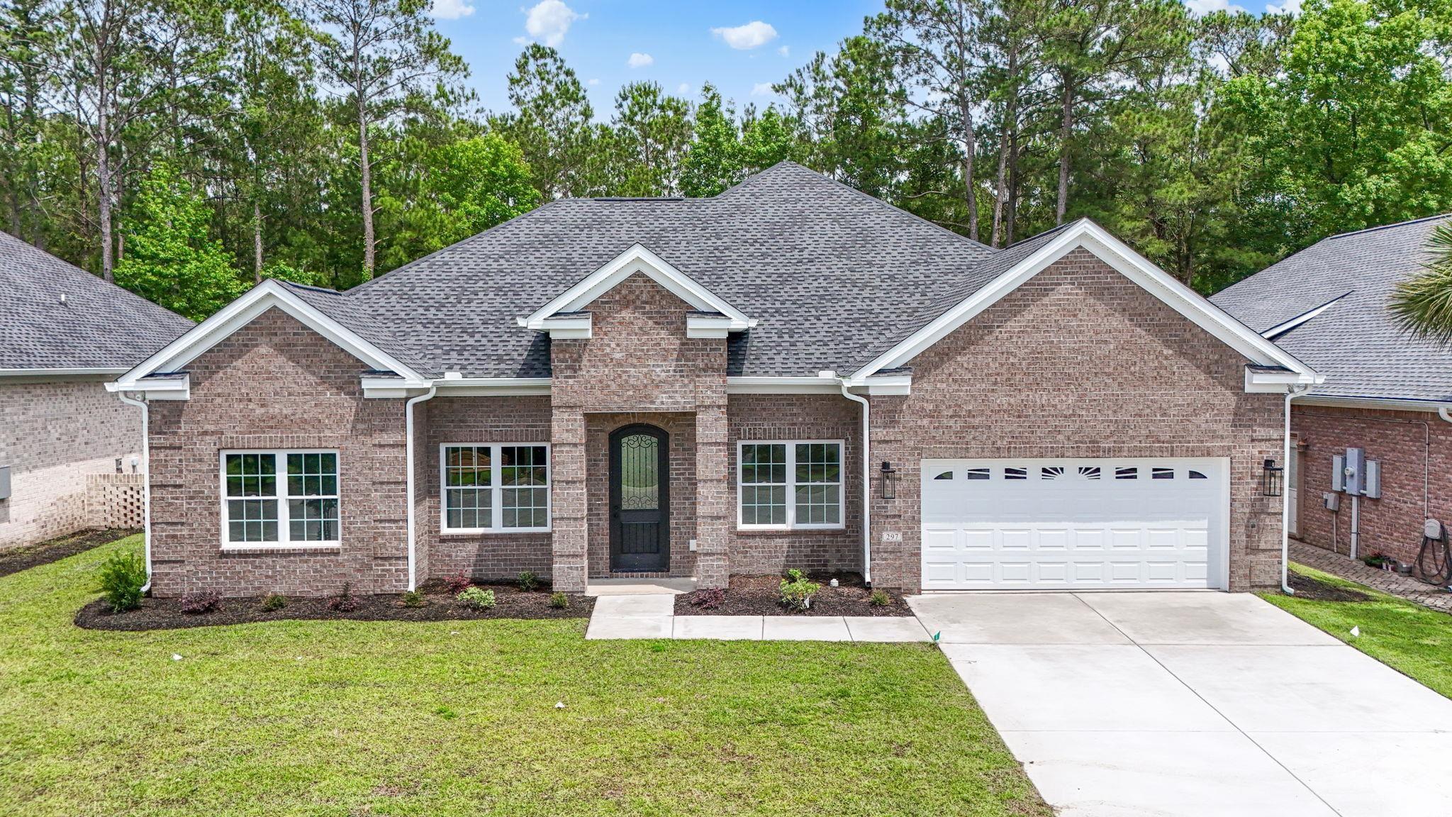 View of front of property featuring an attached garage, roof with shingles, concrete driveway, brick siding, and a front yard
