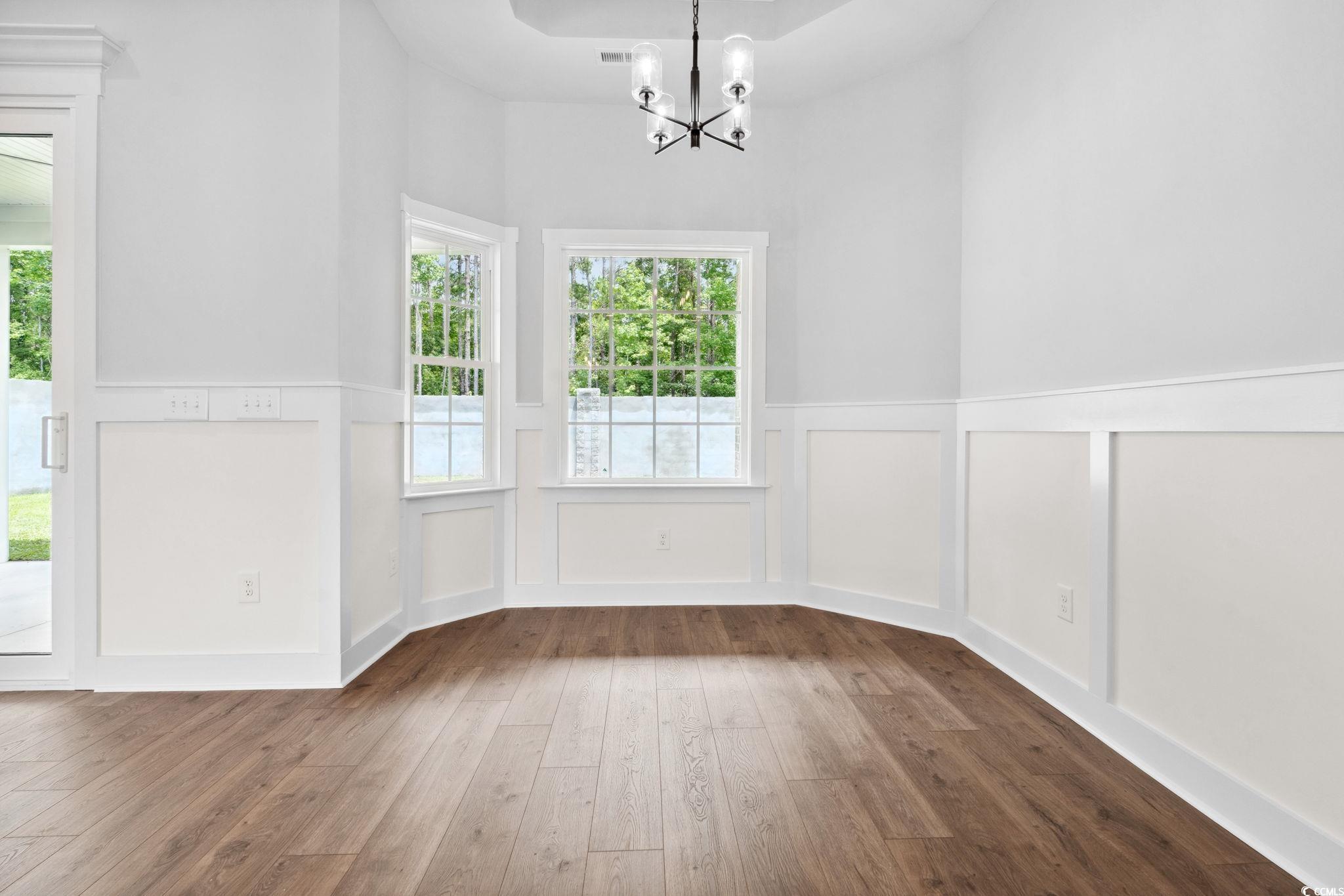297 Waterfall Circle Little River, SC 29566 - Photo 16 of 40 Unfurnished dining area with a chandelier, hardwood / wood-style flooring, wainscoting, a decorative wall, and healthy amount of natural light