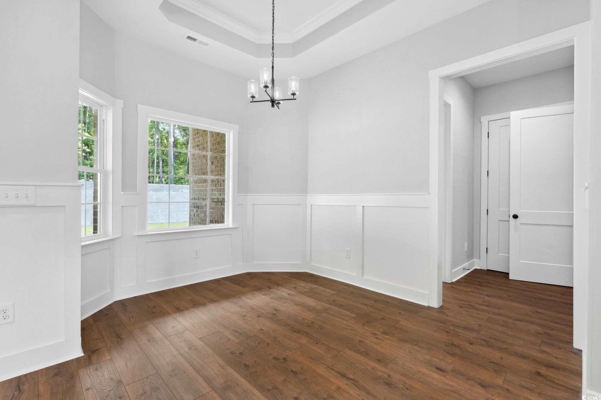 297 Waterfall Circle Little River, SC 29566 - Photo 17 of 40 Unfurnished dining area with dark wood finished floors, a chandelier, a wainscoted wall, crown molding, and a decorative wall