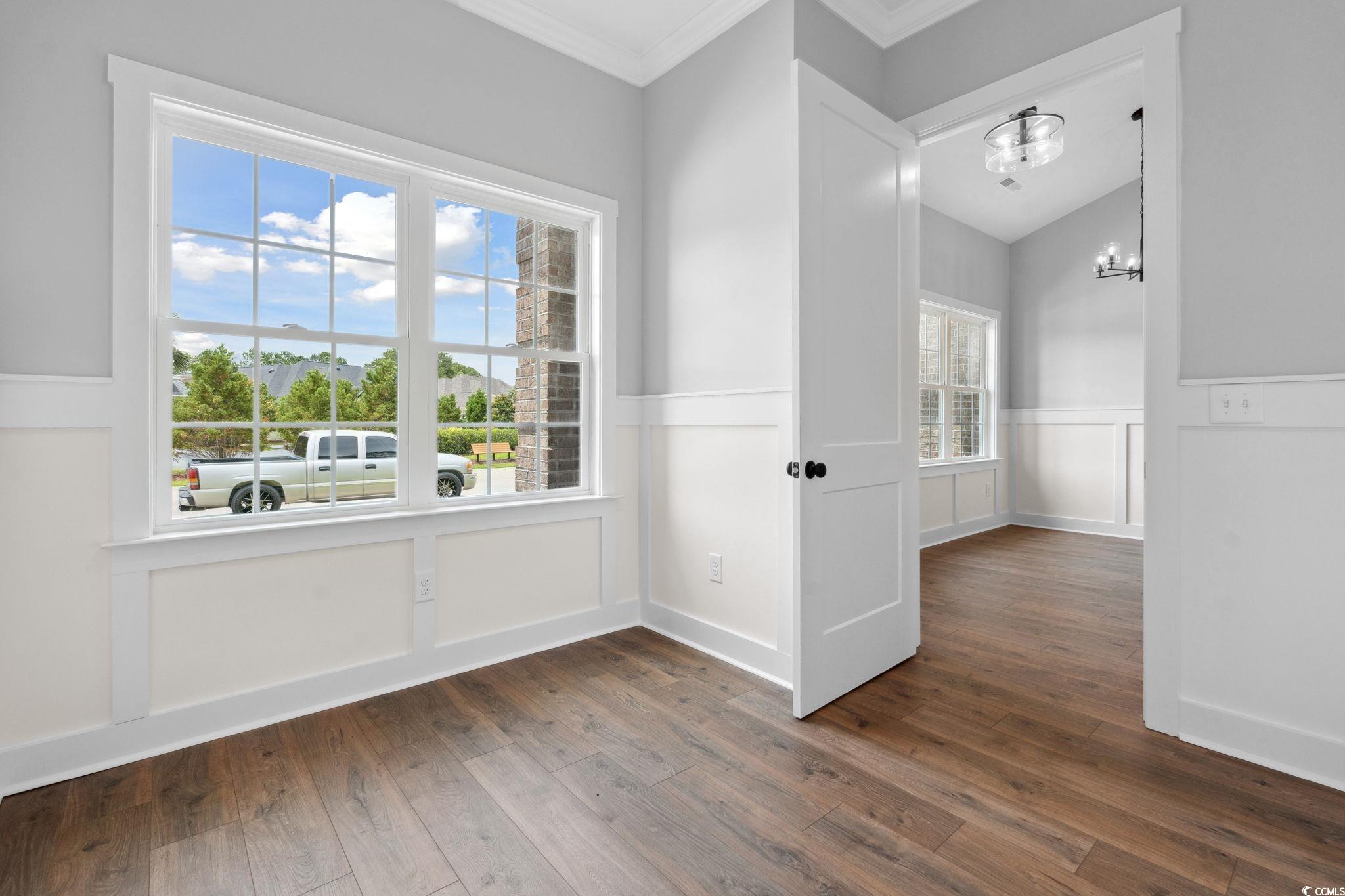297 Waterfall Circle Little River, SC 29566 - Photo 5 of 40 Spare room featuring a chandelier, ornamental molding, a wainscoted wall, dark wood-type flooring, and a decorative wall