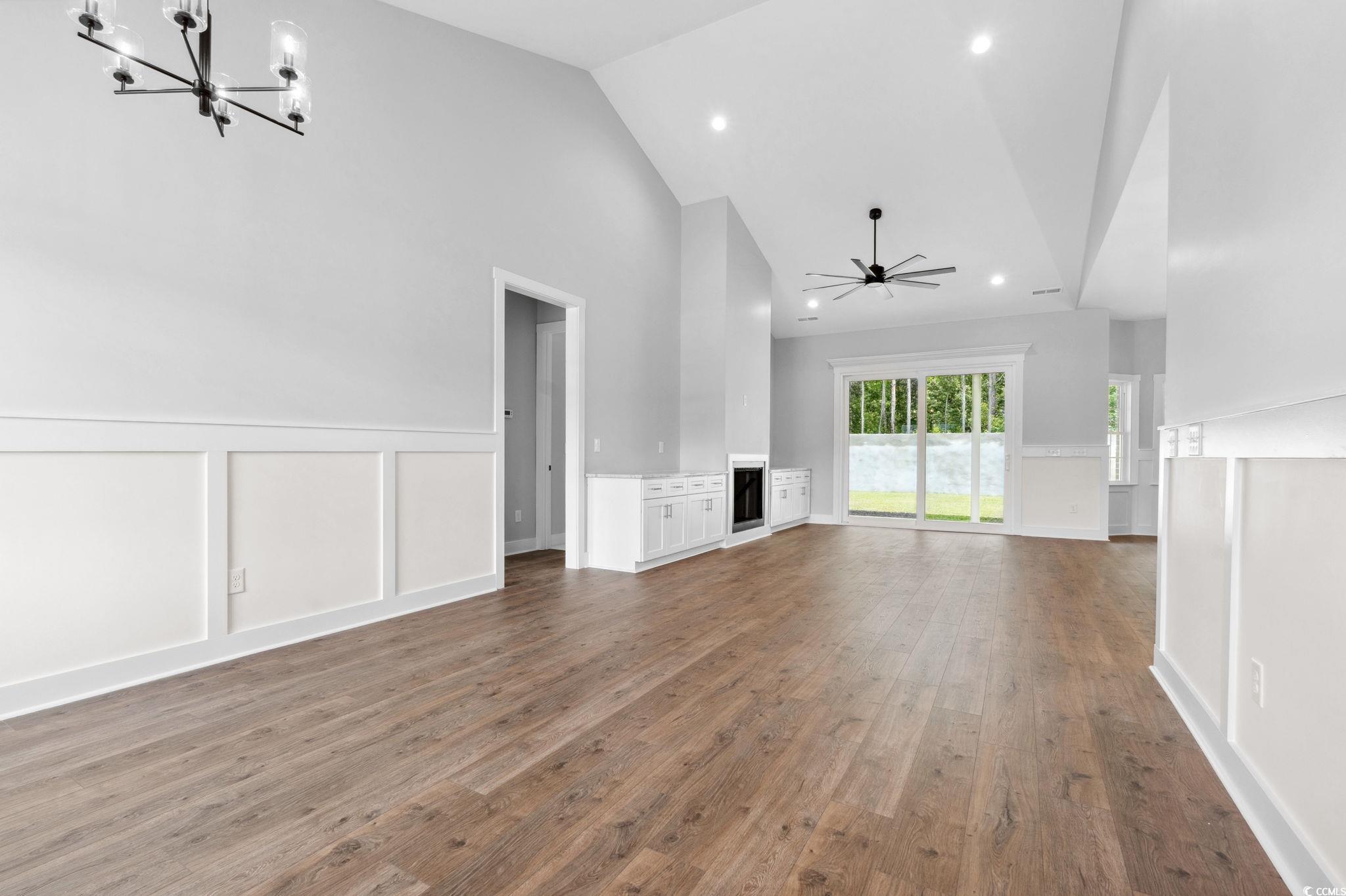 297 Waterfall Circle Little River, SC 29566 - Photo 6 of 40 Unfurnished living room featuring a chandelier, high vaulted ceiling, wood finished floors, wainscoting, and a decorative wall