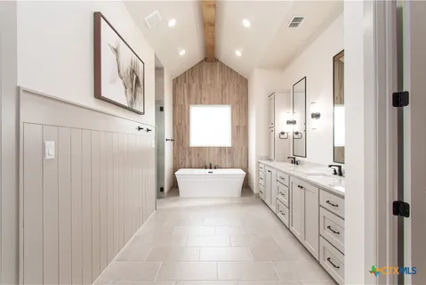 a large white bathroom with a double vanity sink a large mirror and a bathtub