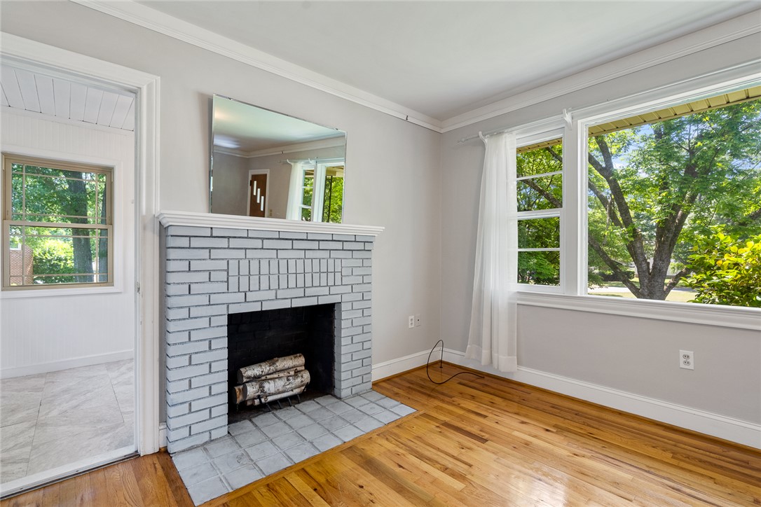 1509 869 Anderson, SC 29621 - Photo 7 of 45 A classic brick fireplace with a wide hearth anchors a bright living space, complemented by generous windows framing leafy outdoor views.