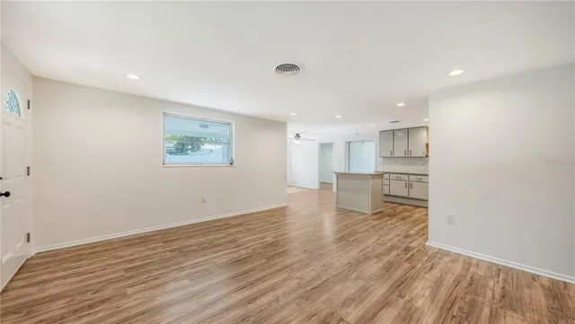a view of empty room with wooden floor and kitchen