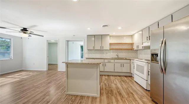 a kitchen with stainless steel appliances granite countertop a refrigerator a sink dishwasher a stove and white countertops with wooden floor