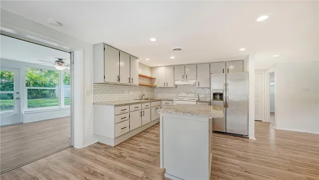 a kitchen with stainless steel appliances granite countertop a refrigerator a sink dishwasher a stove and white cabinets with wooden floor