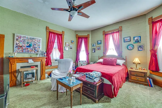 a bedroom with a bed a standing fan and a bookshelf