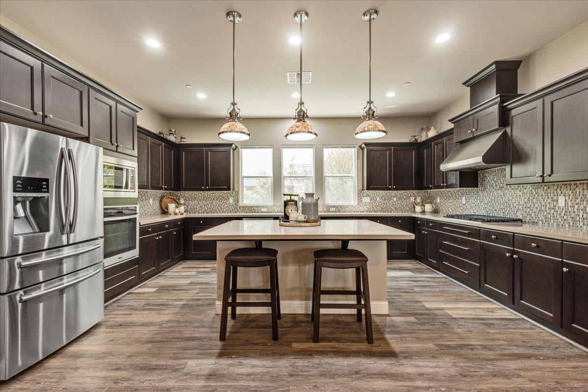 a kitchen with stainless steel appliances granite countertop a sink a stove a refrigerator and island with wooden floor