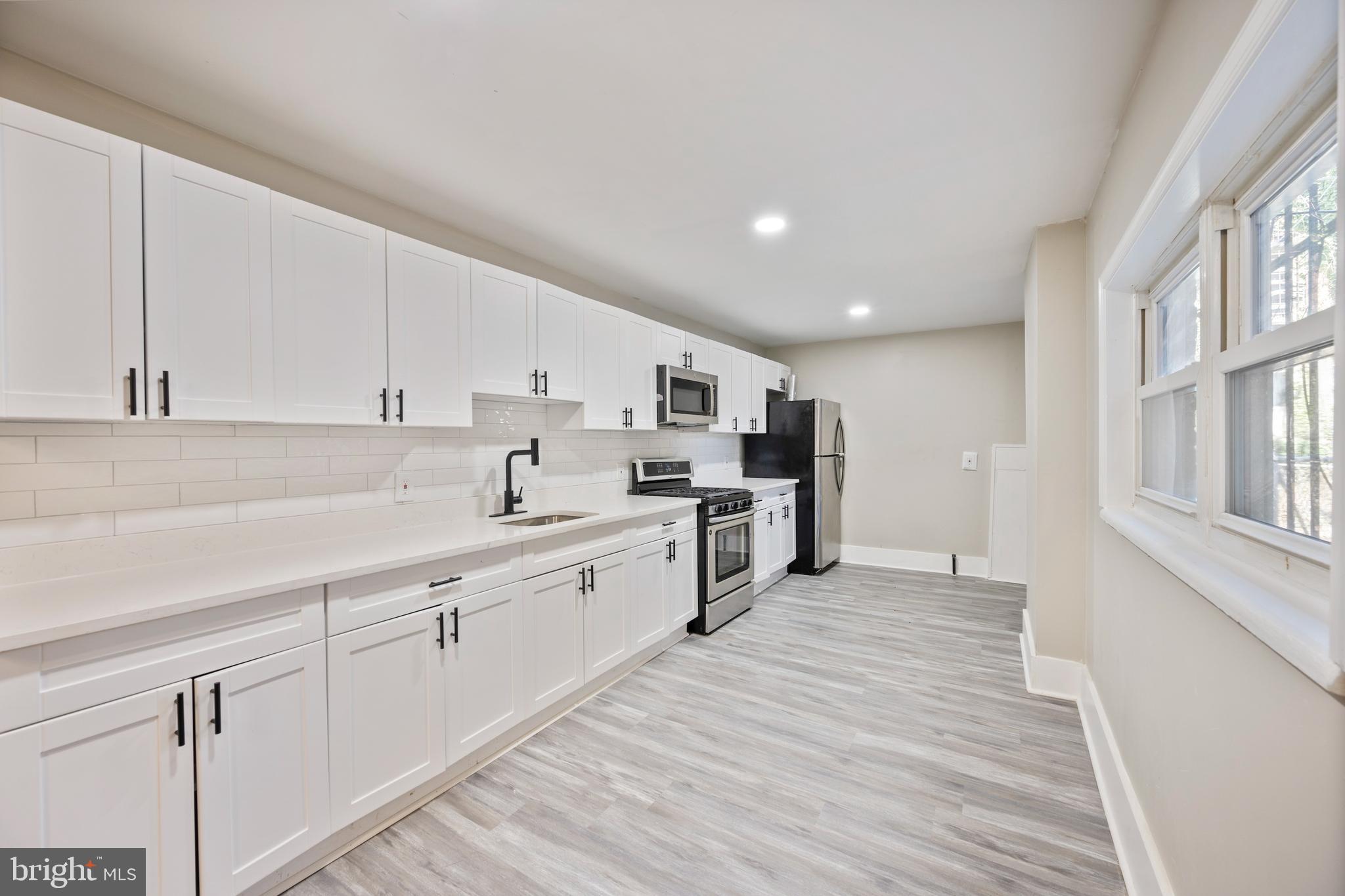1038 Brantley Avenue Baltimore, MD 21217 - Photo 16 of 38 a large white kitchen with stainless steel appliances granite countertop a lot of counter space and wooden floors