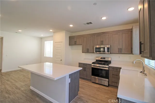 a large kitchen with stainless steel appliances a large counter top a stove a sink a refrigerator and a window