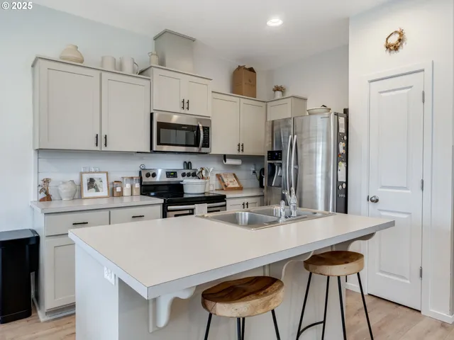 a kitchen with stainless steel appliances a stove a sink dishwasher a refrigerator with a dining table and chairs