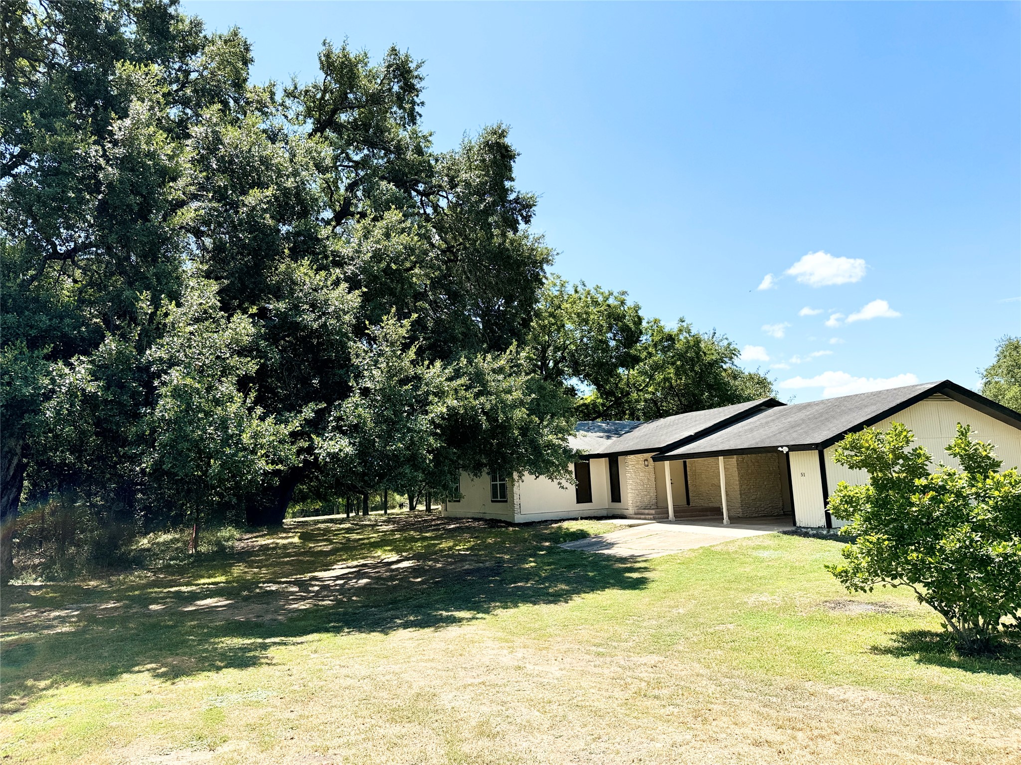 Ranch-style residence featuring a broad carport, dark shingle roofing, and light-colored siding