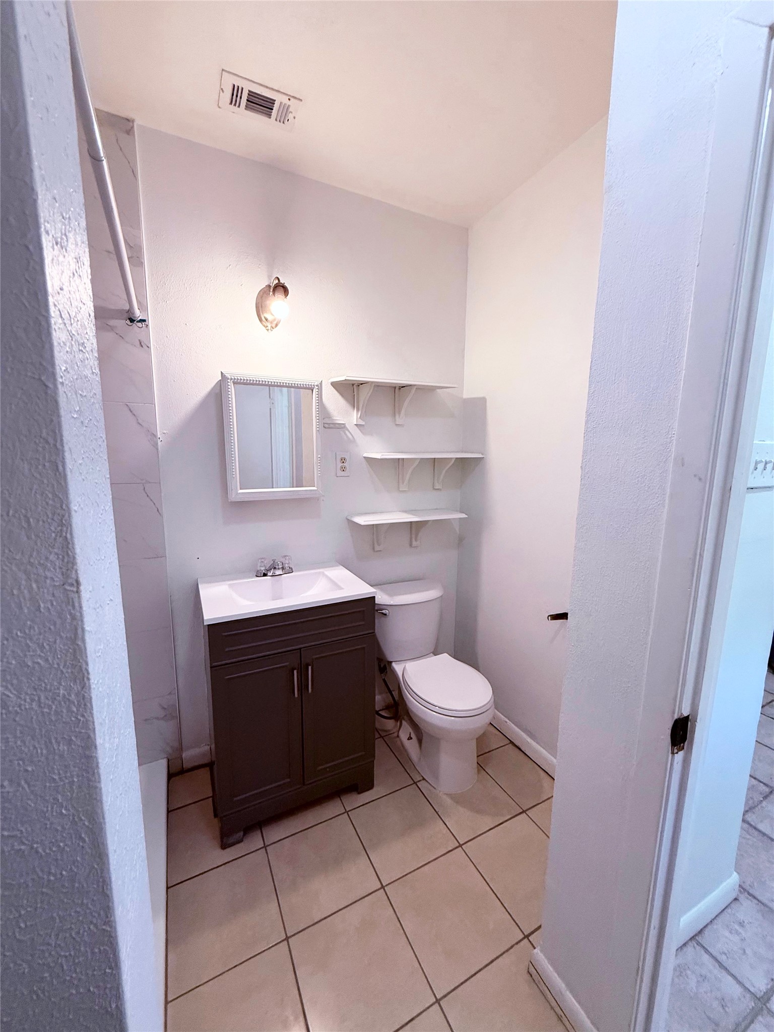 51 Hanging Oak Road Dale, TX 78616 - Photo 13 of 32 Bathroom featuring a dark wood-finish vanity with an integrated white sink, a wall-mounted mirror, and complementary open shelving