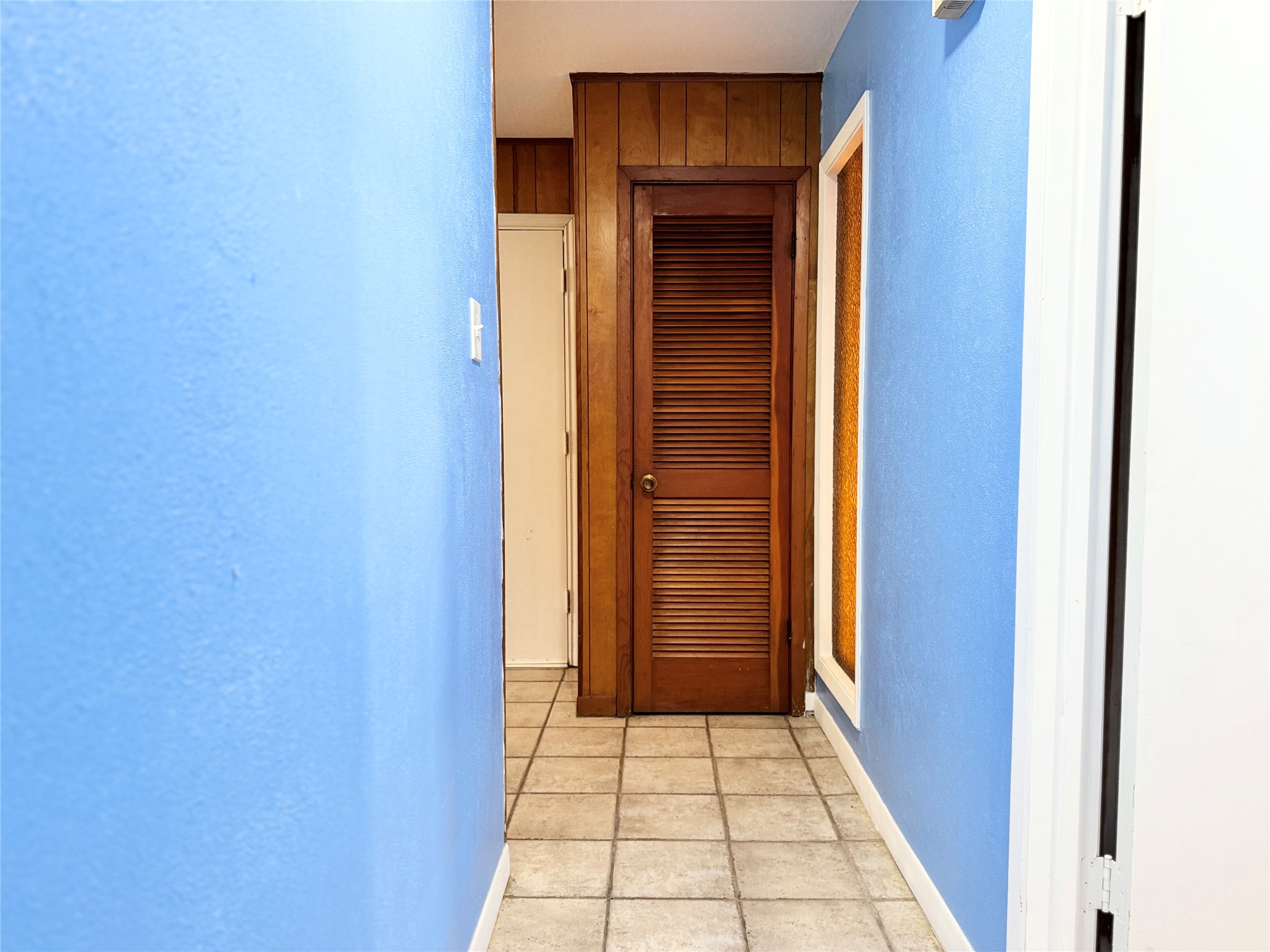 51 Hanging Oak Road Dale, TX 78616 - Photo 22 of 32 Hallway featuring blue wall paint, square tile flooring, wood paneling, a louvered wood door, and white trim accents
