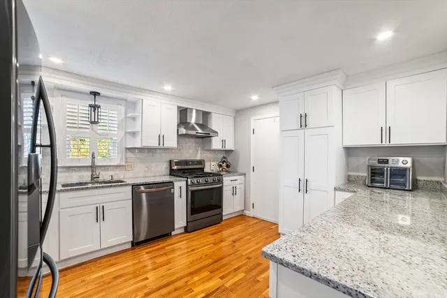 a kitchen with stainless steel appliances granite countertop a stove top oven a sink dishwasher a refrigerator and white cabinets with wooden floor