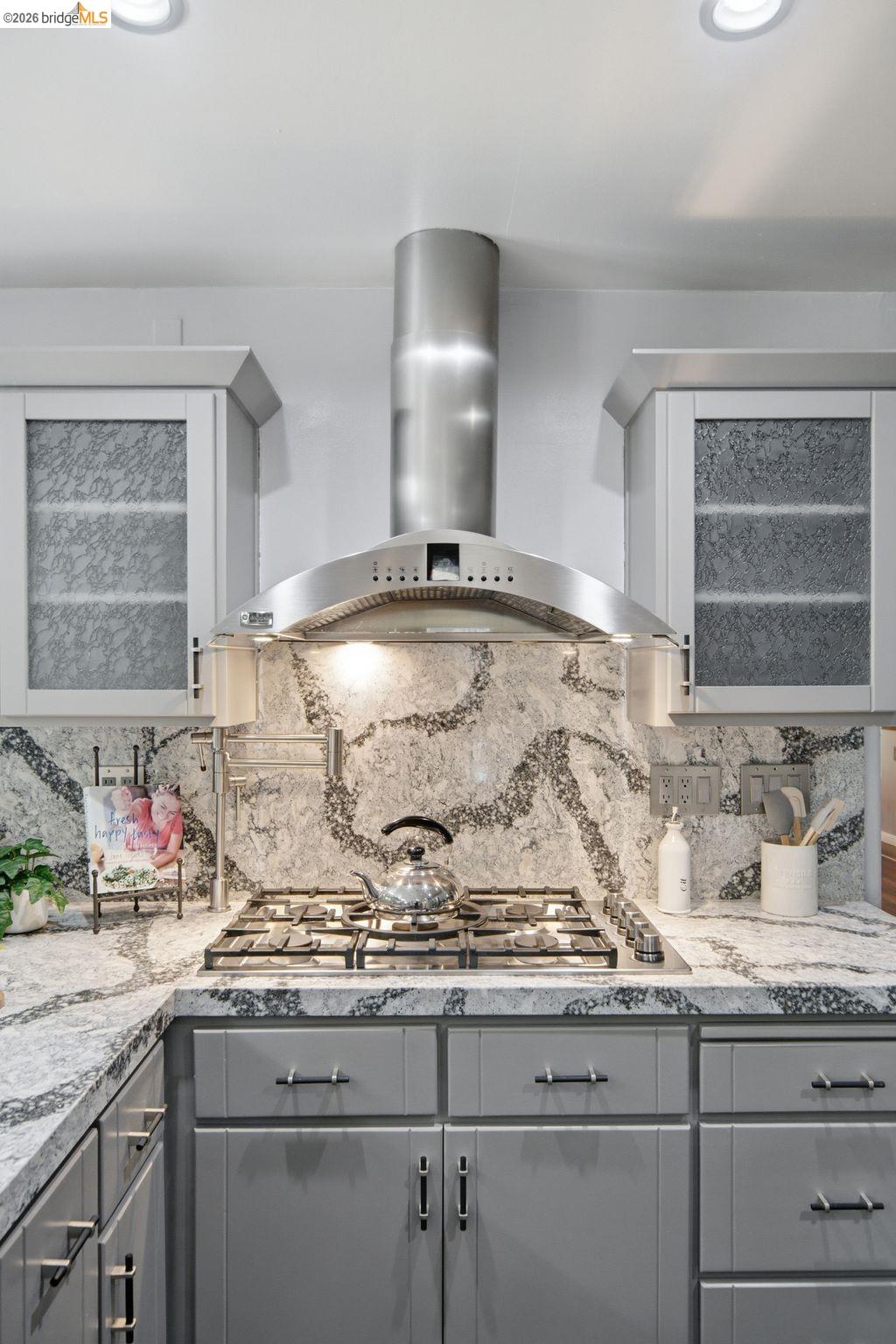 11133 Golf Links Road Oakland, CA 94605 - Photo 15 of 57 Kitchen featuring a stainless steel range hood, built-in gas cooktop, patterned countertop and backsplash, and light gray cabinetry with dark hardware
