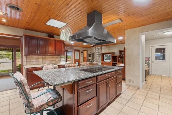 a view of a kitchen with kitchen island granite countertop lots of wooden cabinets a sink and appliances