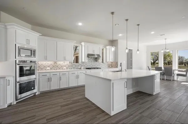 a large white kitchen with stainless steel appliances granite countertop a stove a sink a refrigerator and white cabinets with wooden floor