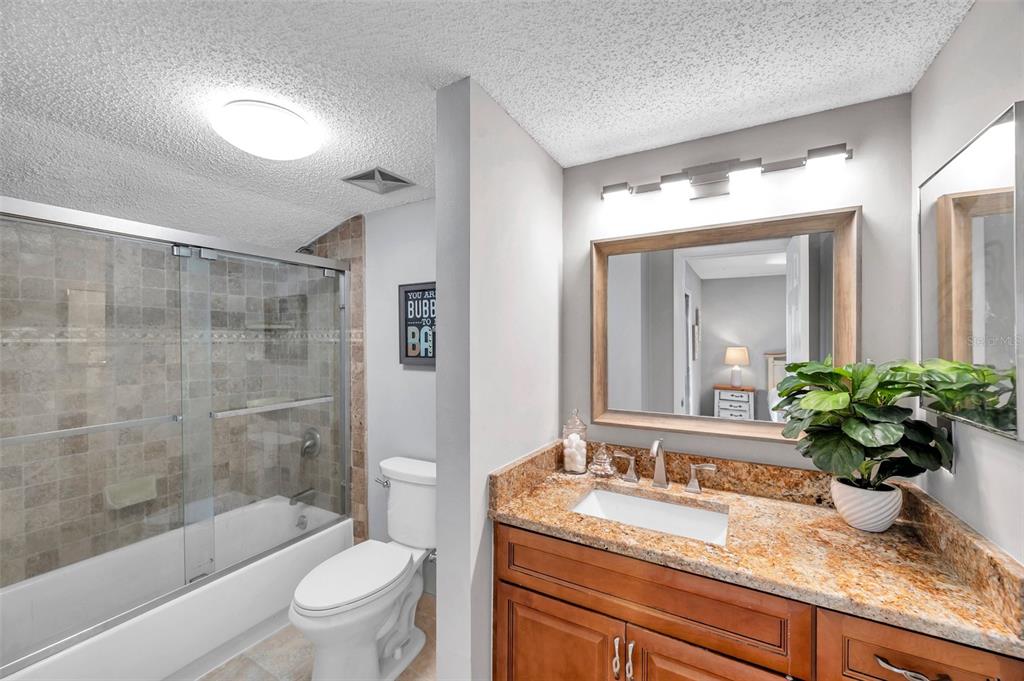 6311 Newtown Circle, Unit 11B1 Tampa, FL 33615 - Photo 28 of 49 a bathroom with a granite countertop sink a toilet a mirror a vanity a bathtub and shower