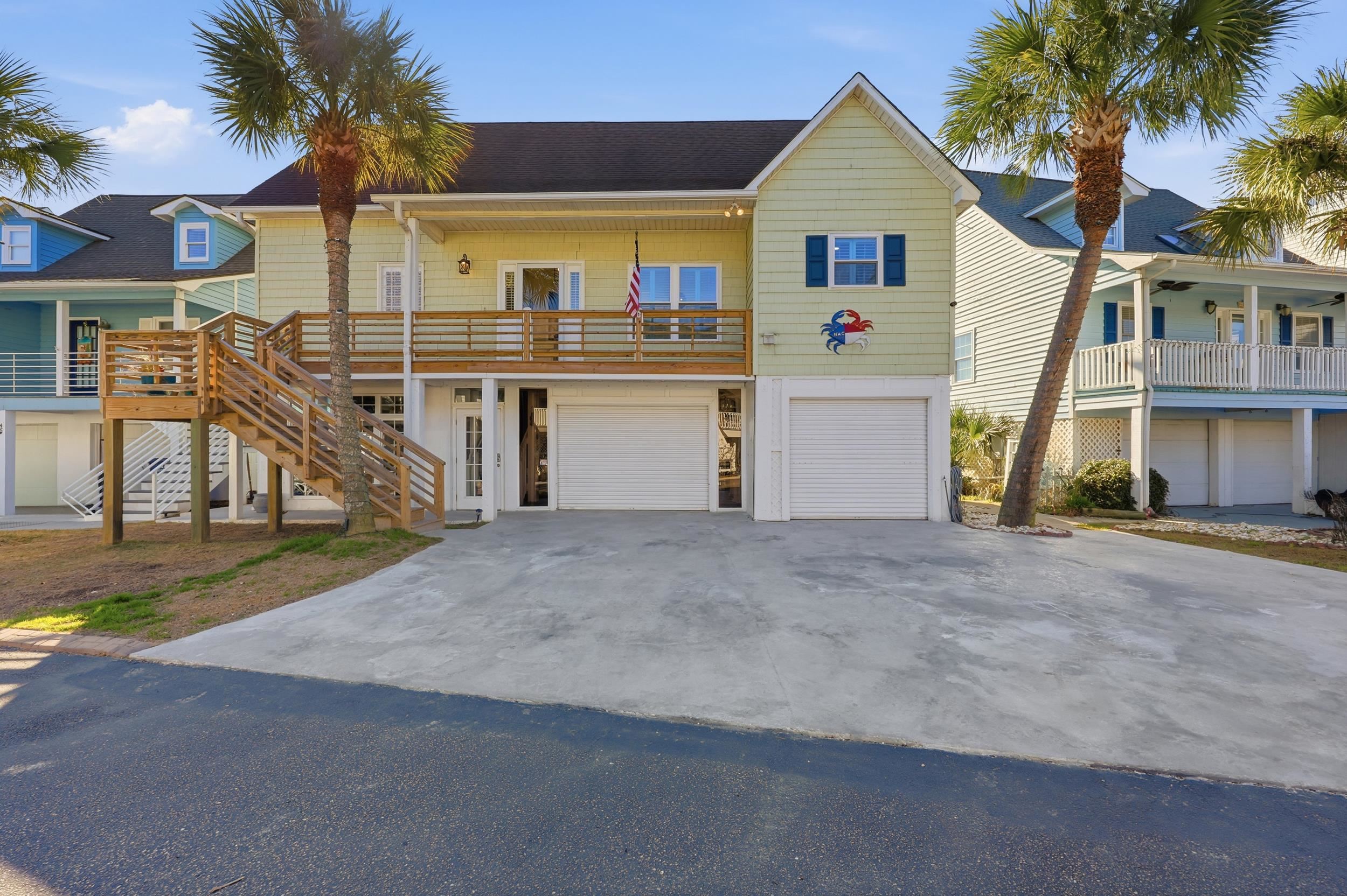 Coastal home featuring an attached garage, stairway, driveway, and a shingled roof