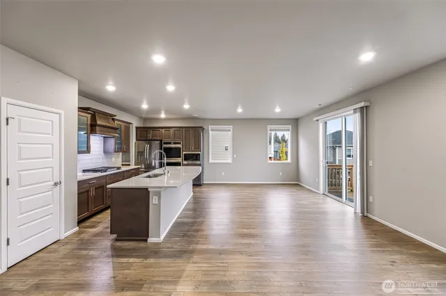 a kitchen with stainless steel appliances kitchen island granite countertop a stove top oven a sink dishwasher a refrigerator and a dining table with wooden floor