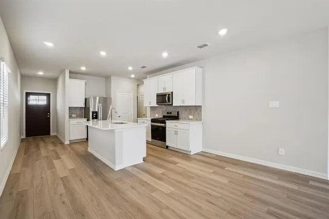 a view of a kitchen with kitchen island a sink wooden floor and white stainless steel appliances
