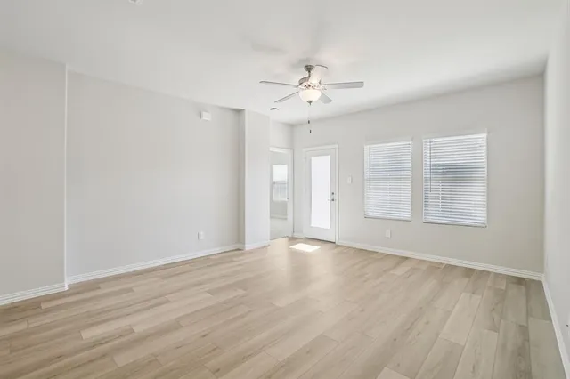 an empty room with wooden floor chandelier fan and windows