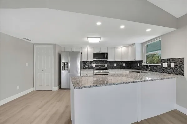 a kitchen with granite countertop white cabinets stainless steel appliances and a window
