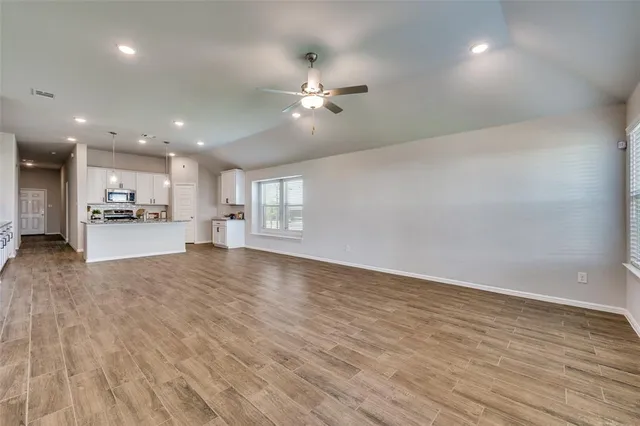 an empty room with wooden floor kitchen view and a window